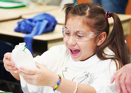 An elementary school student is excited by the chemical reaction from her Science Explorers experiment